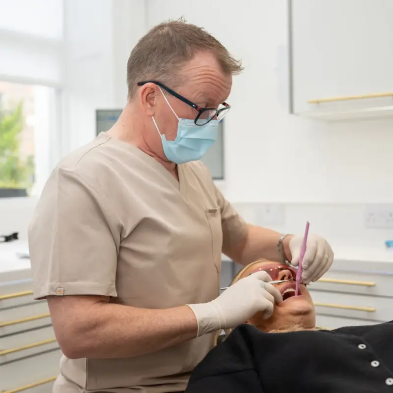 Dr Barry Oulton in scrubs, mask and gloves, treating a patient reclined in the dental chair.