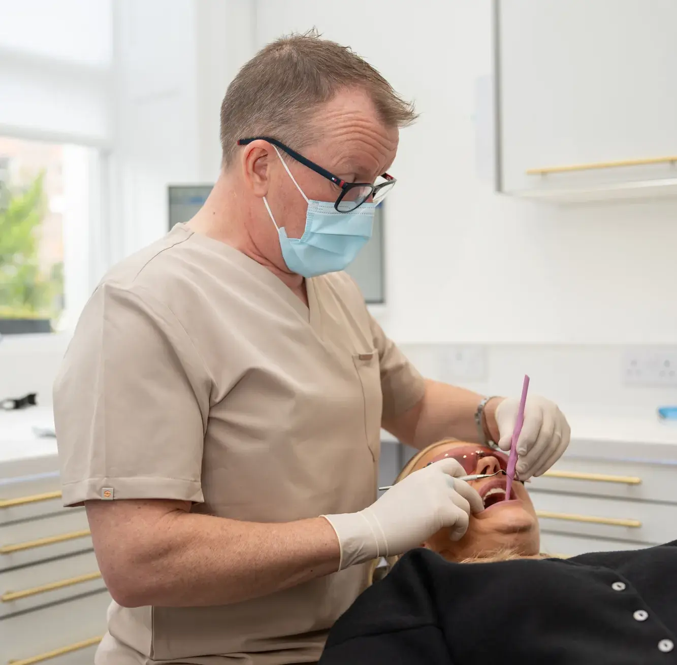 Dr Barry Oulton in scrubs, mask and gloves, treating a patient reclined in the dental chair.